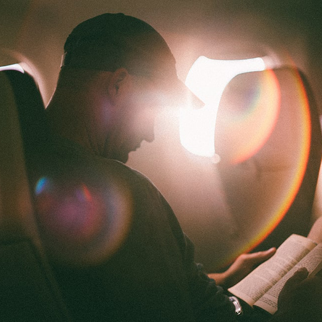 A man relaxing and reading a book while flying.